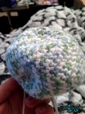 A photo of an unstuffed crochet sphere in green and white yarn.