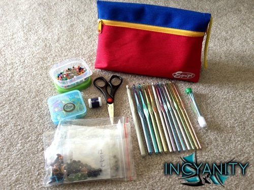 Various crochet tools, including hooks, safety eyes, stitch markers, scissors, a row counter, pins, and darning needles, all to be kept in a pencil case.